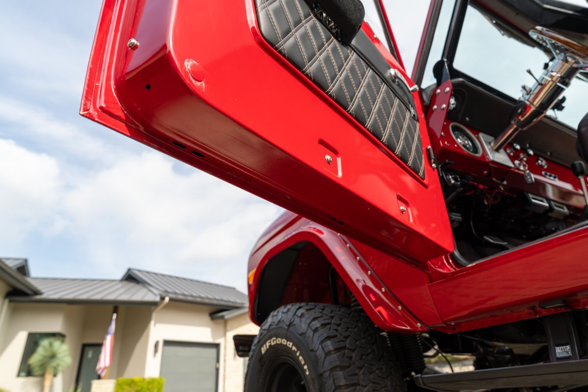 Red 1966 Ford Bronco interior with diamond-stitched door panel trim and chrome steering wheel.
