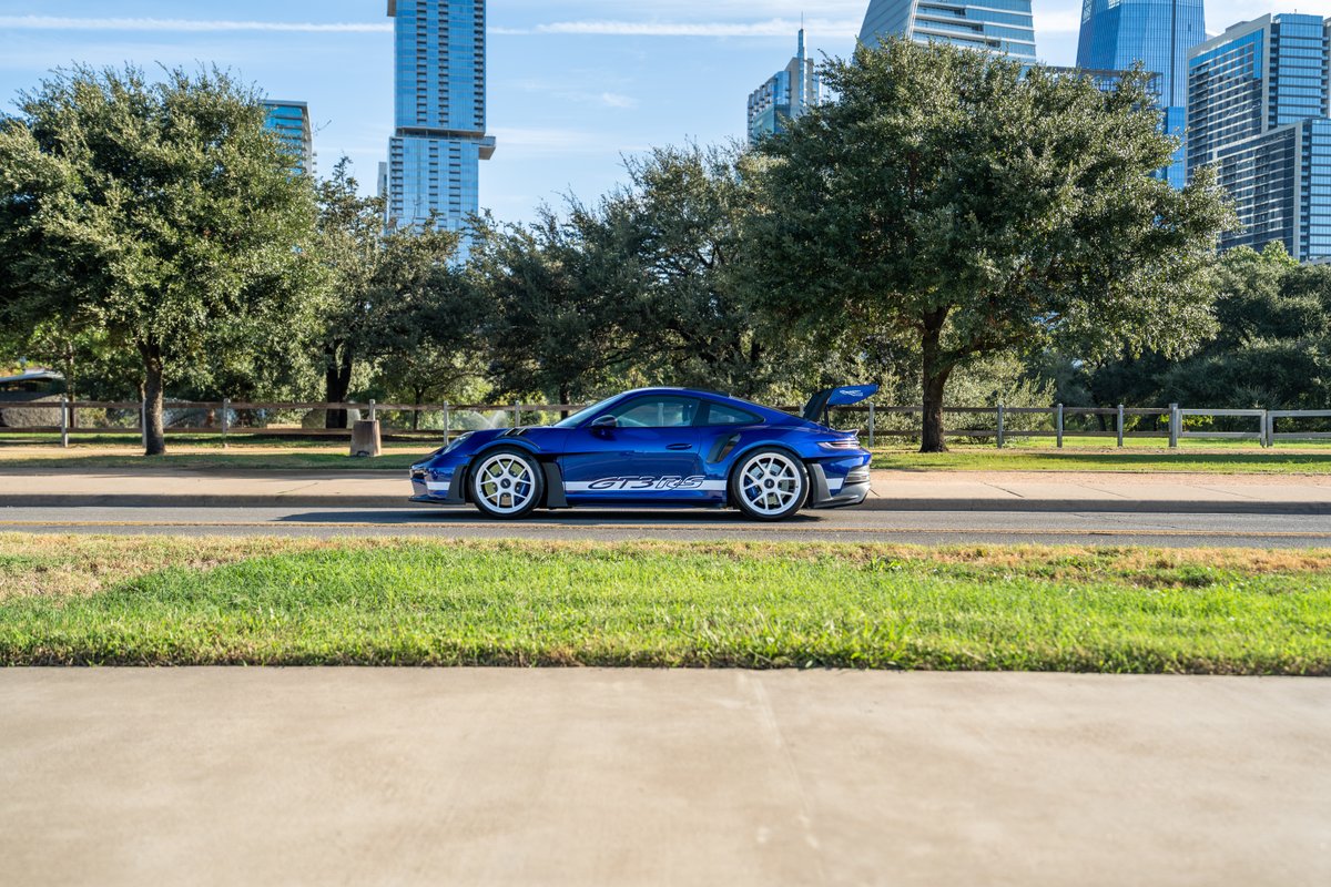 Blue 2025 Porsche 911 GT3 RS with white livery and white rims parked curbside.