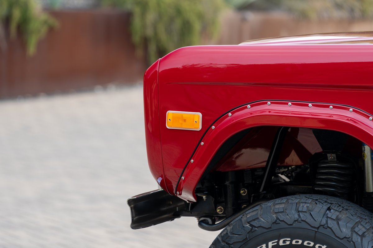 Close-up of a red 1966 Ford Bronco fender with rivets, amber marker light, and tire.