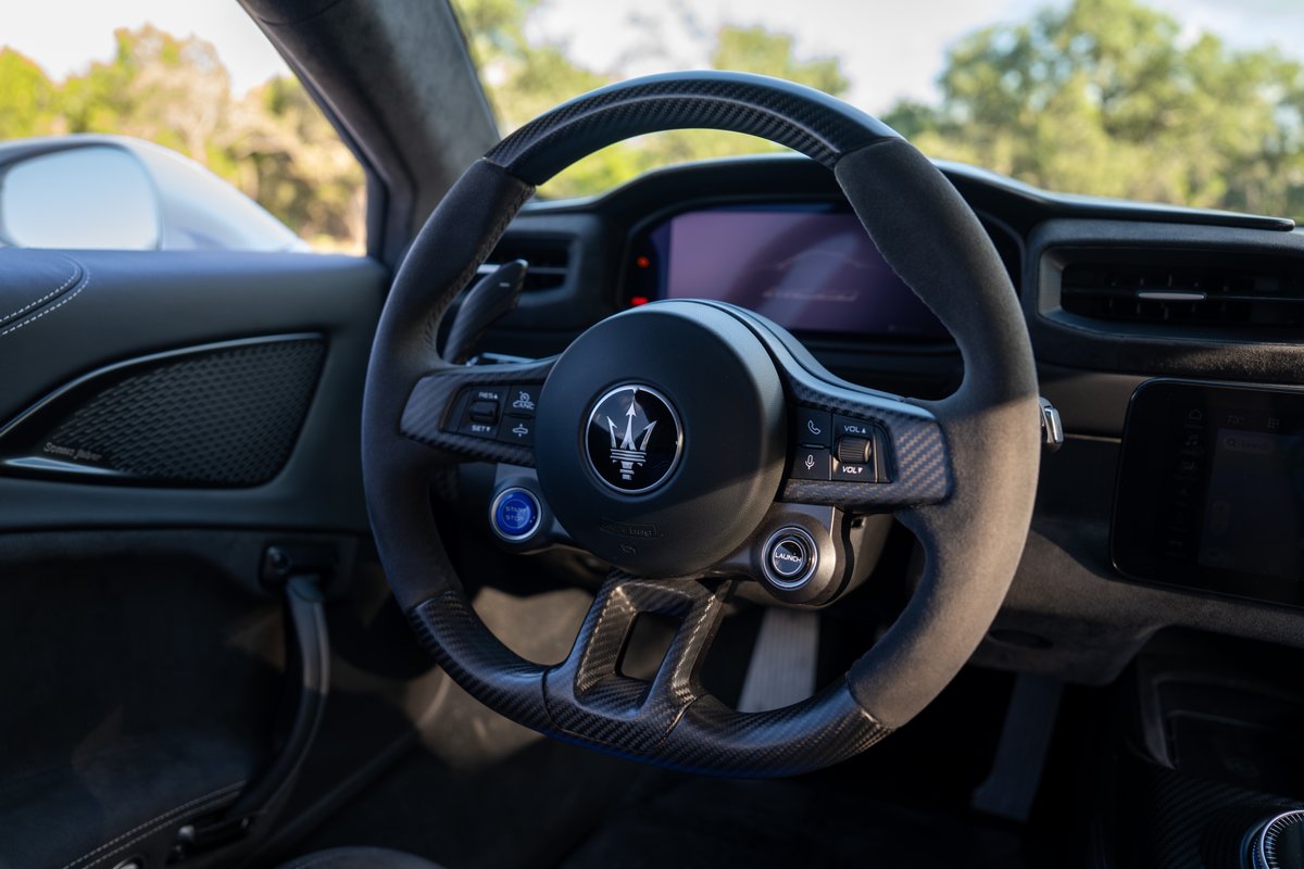 Close-up of the 2024 Maserati MC20 Icona steering wheel with carbon fiber trim and Trident logo.