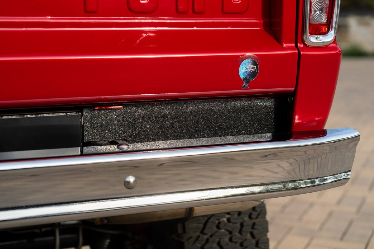 Close-up of a red 1966 Ford Bronco's rear with a chrome bumper and textured trim.