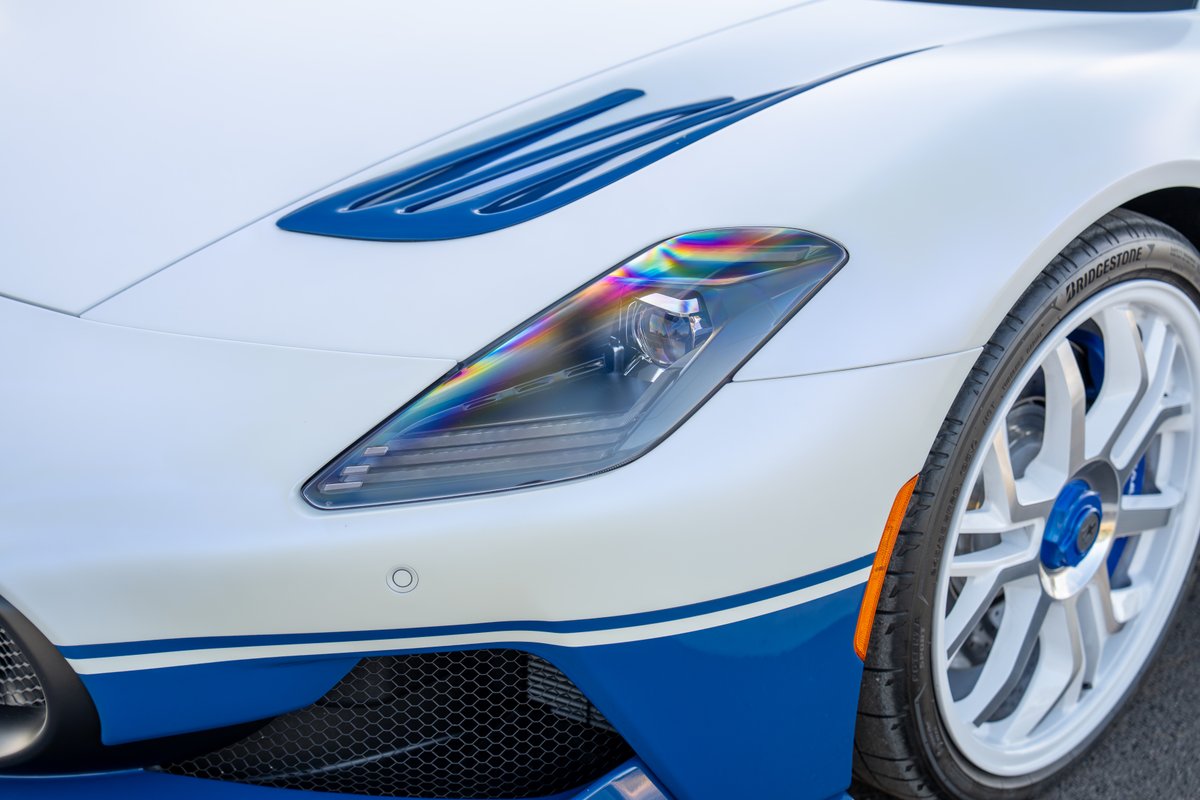 2024 Maserati MC20 Icona in white with blue livery, showing the iridescent headlight and multi-spoke white rims.