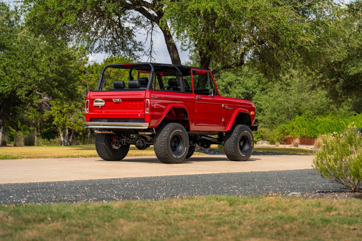 Red 1966 Ford Bronco by Atlas Broncos, with lifted suspension, black rims, and off-road tires.