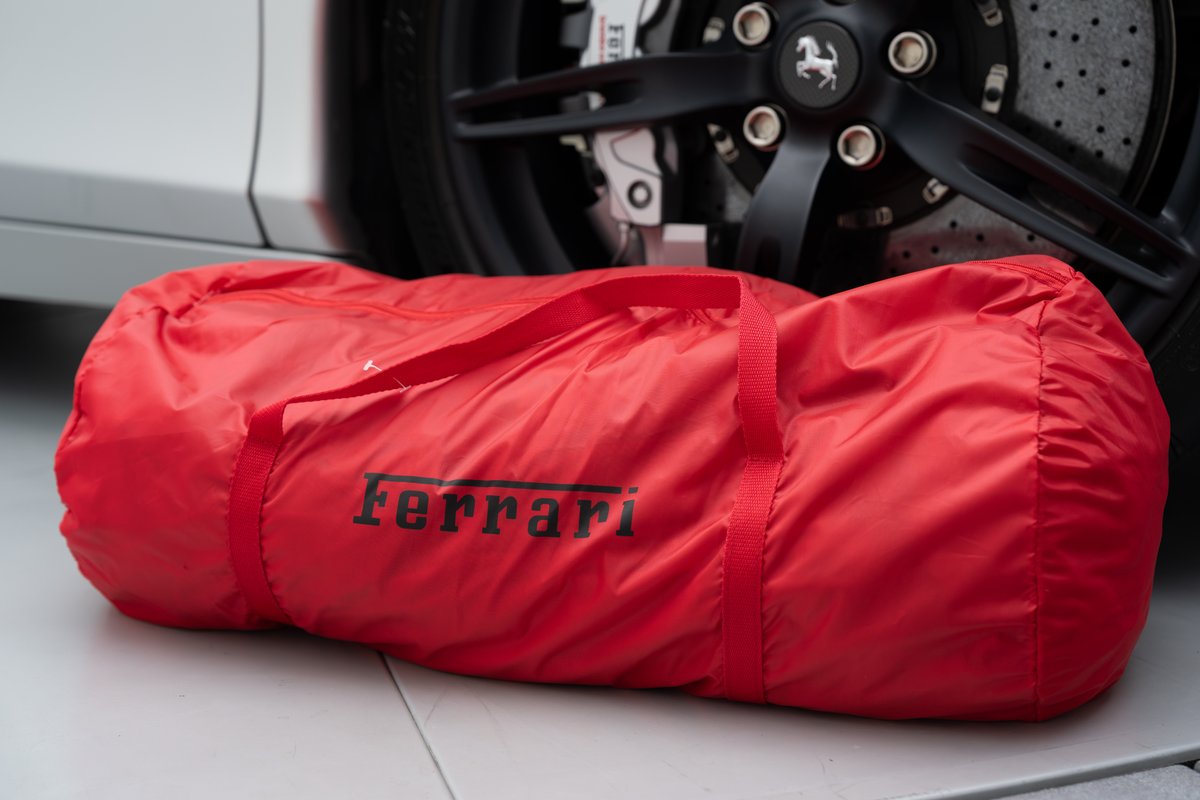 Red Ferrari 458 Speciale with black rims and the Ferrari logo on a red duffel bag.