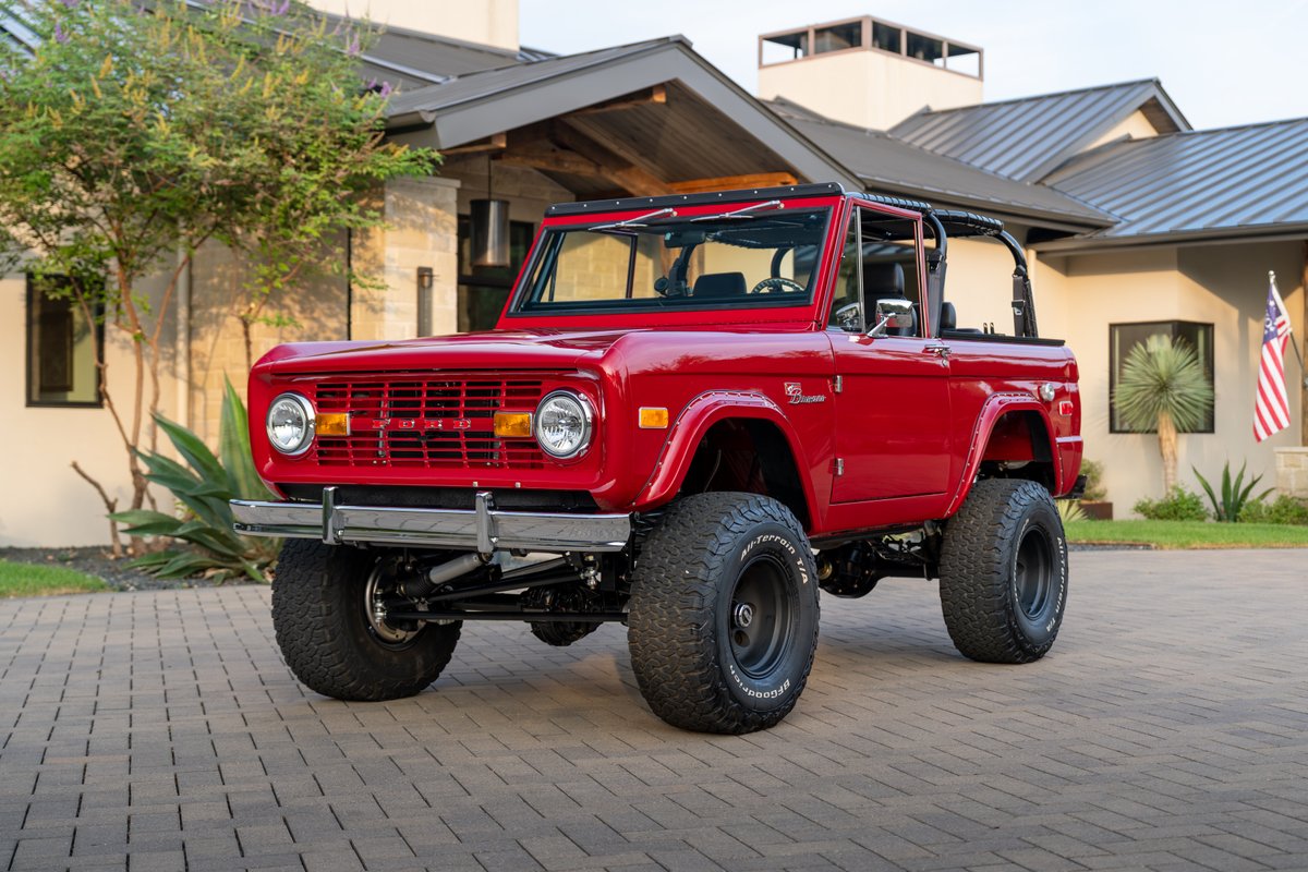 Red 1966 Ford Bronco by Atlas Broncos with black rims and off-road tires.