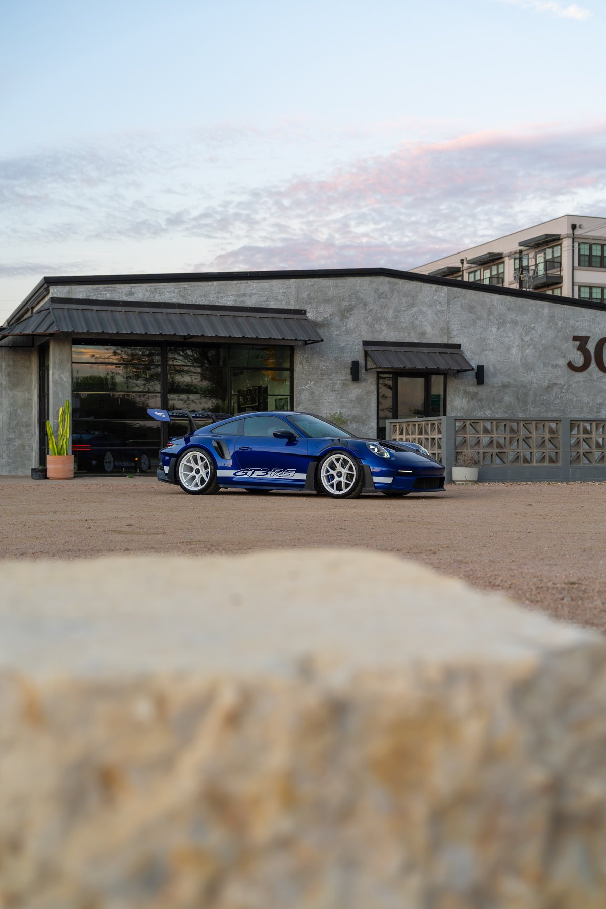 A blue 2025 Porsche 911 GT3 RS with white multi-spoke rims and a white stripe livery.