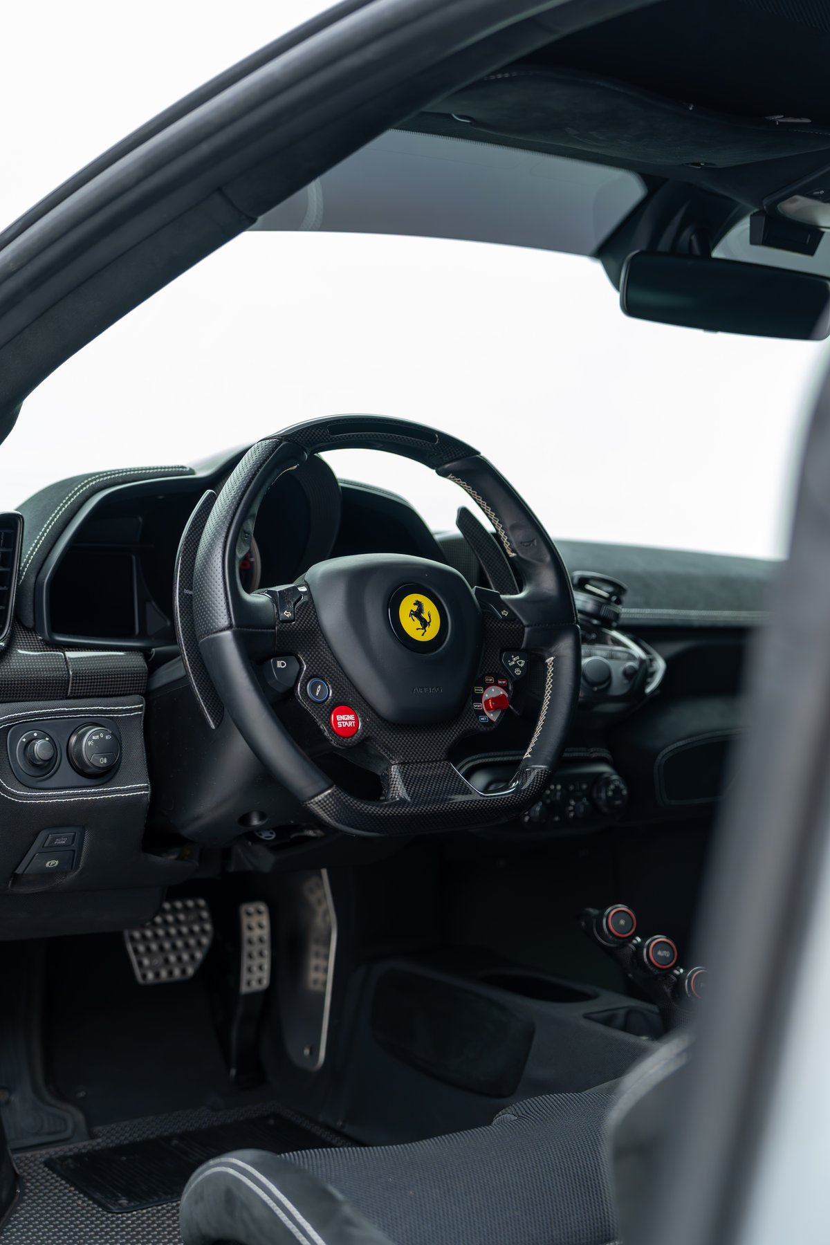 2015 Ferrari 458 Speciale interior with carbon fiber steering wheel, yellow Ferrari emblem, and red engine start button.