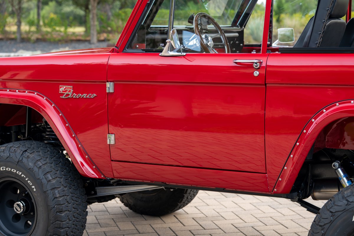 Red 1966 Ford Bronco by Atlas Broncos, showing the driver side door, riveted fender flares, and off-road tires.