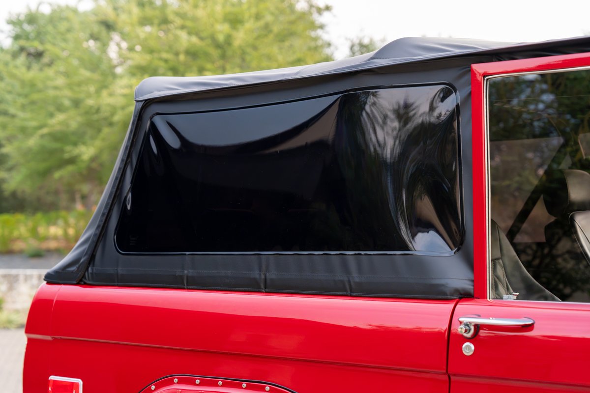 1966 red Ford Bronco with a black soft top and tinted rear window.