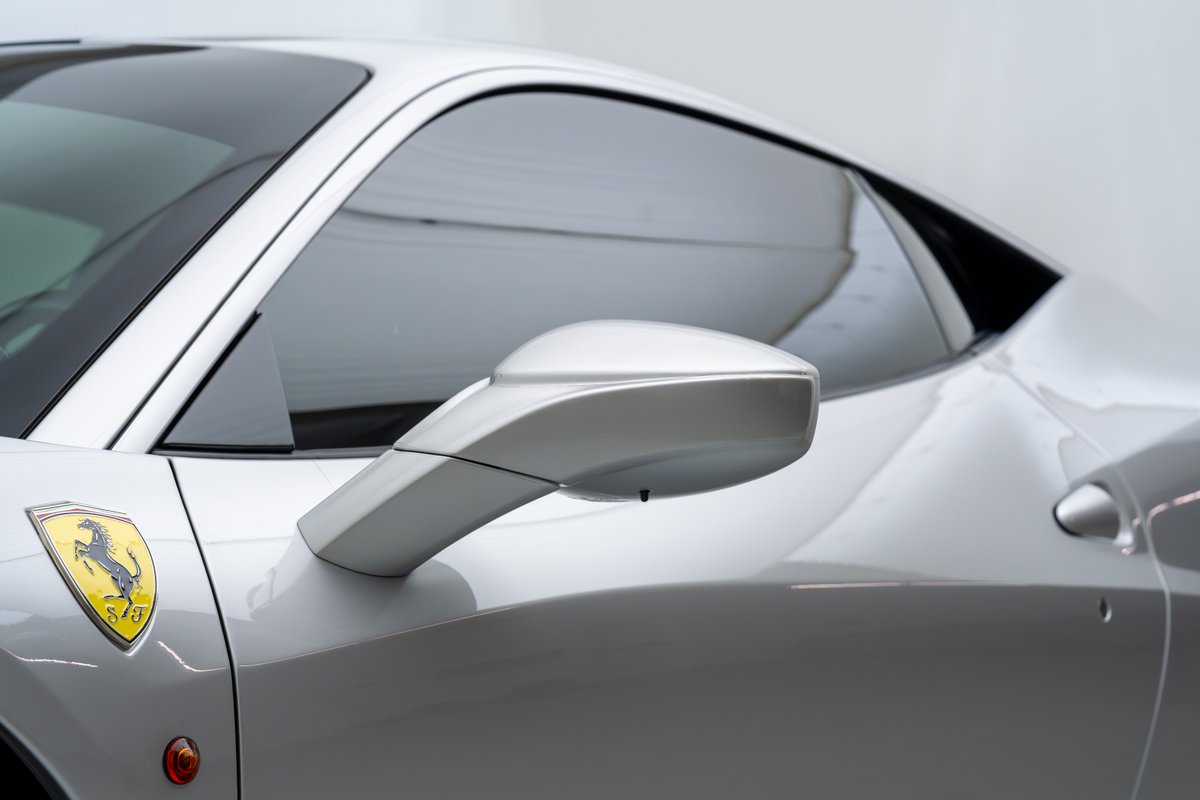 Close-up of a silver 2015 Ferrari 458 Speciale, showing the side mirror and the iconic Prancing Horse badge.
