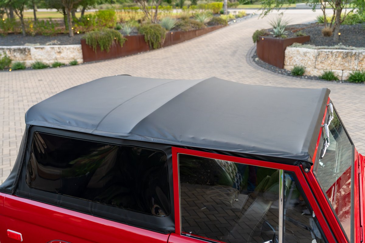 Red 1966 Ford Bronco with a black soft top, featuring clear side windows and chrome trim.