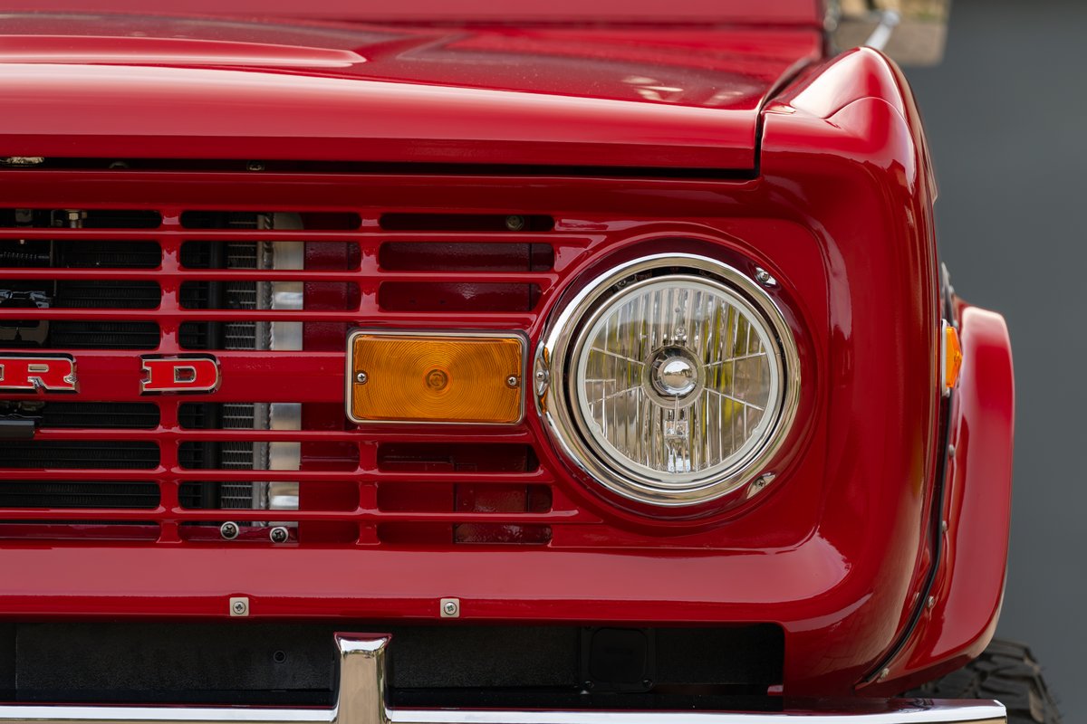 Front view of a red 1966 Ford Bronco's grille, headlight, and amber turn signal.