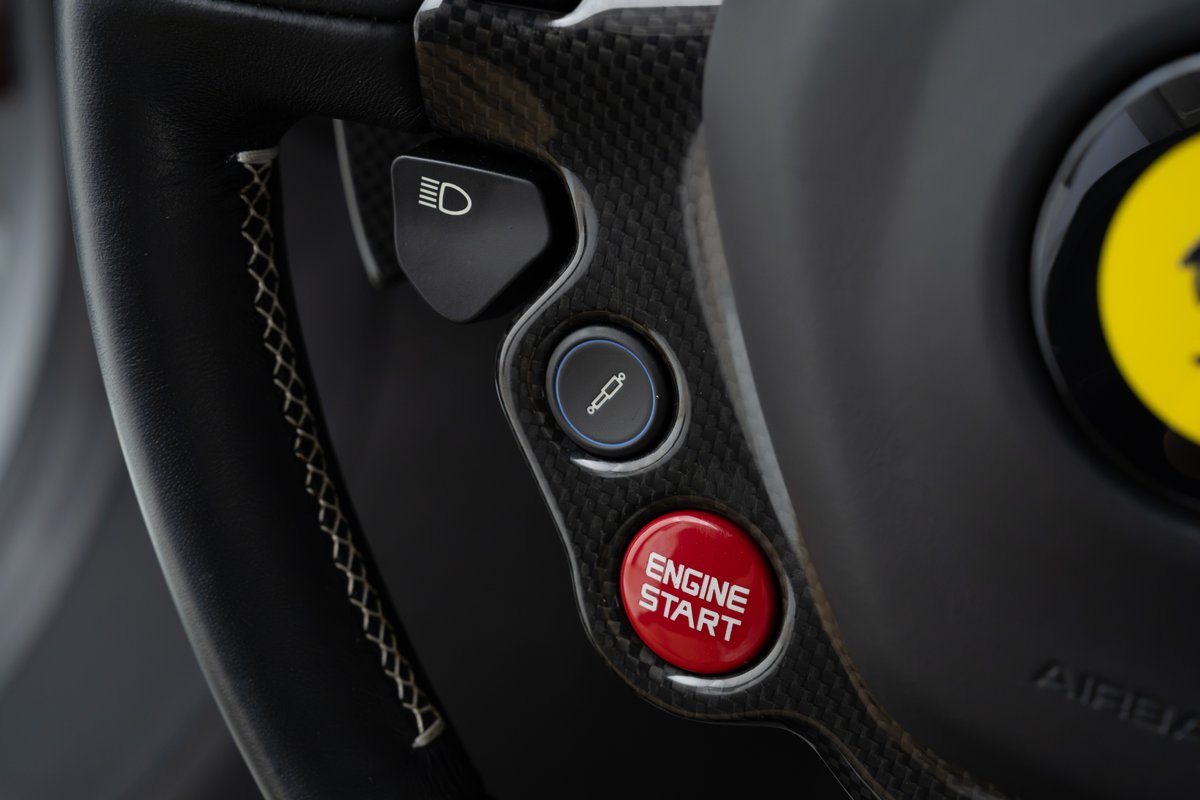 Close-up of a red Ferrari 458 Speciale steering wheel with carbon fiber trim and engine start button.