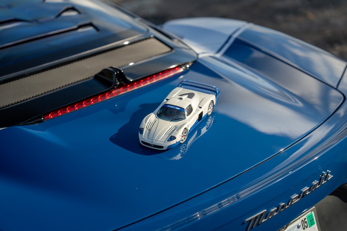 A white and blue Maserati MC20 Icona model rests on the hood of a blue Maserati.