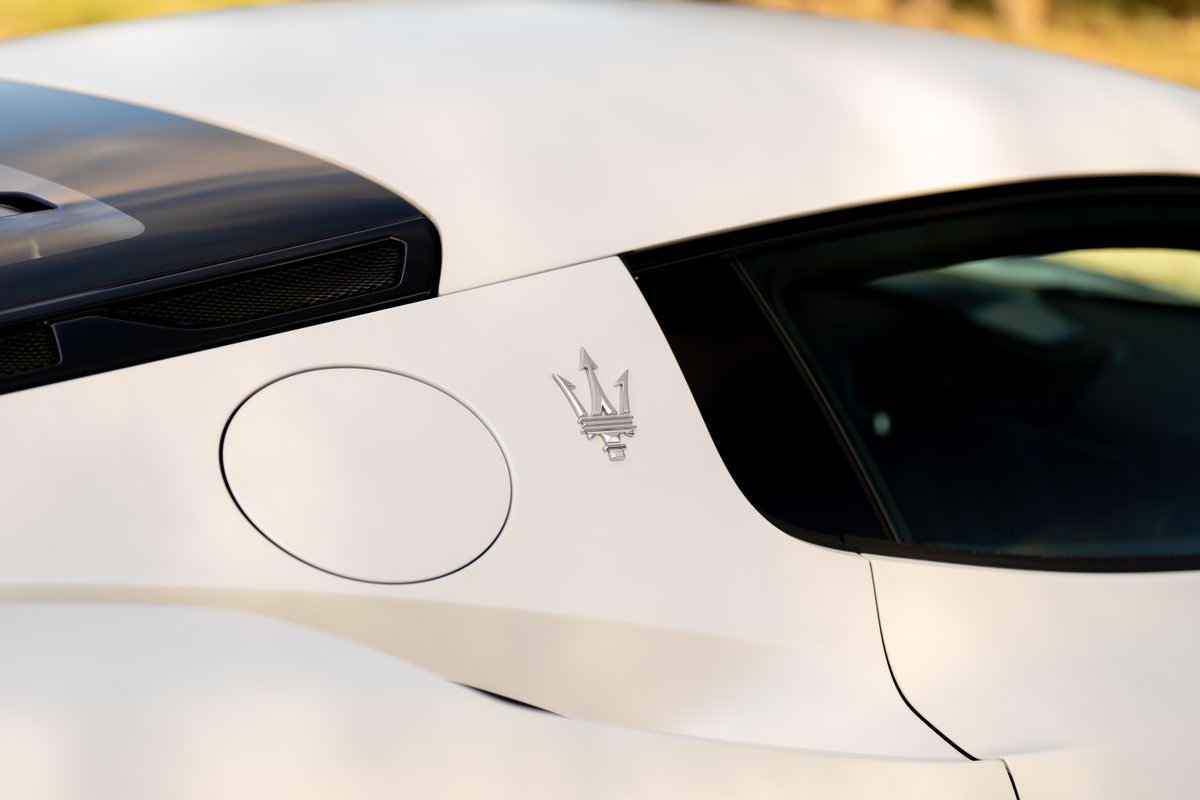 Close-up of the 2024 Maserati MC20 Icona's silver trident badge on white body trim.