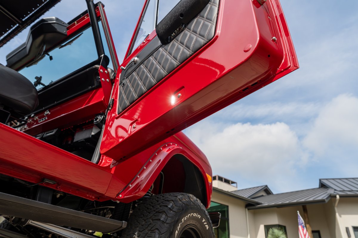 Red 1966 Ford Bronco with diamond-stitched door panel and off-road tires.