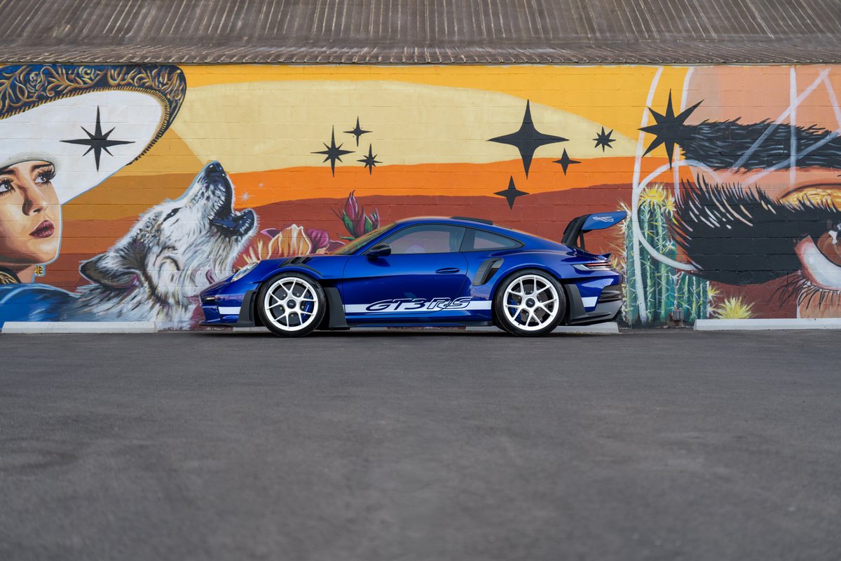 2025 Porsche 911 GT3 RS in blue, with white racing rims and side livery, parked against a mural.