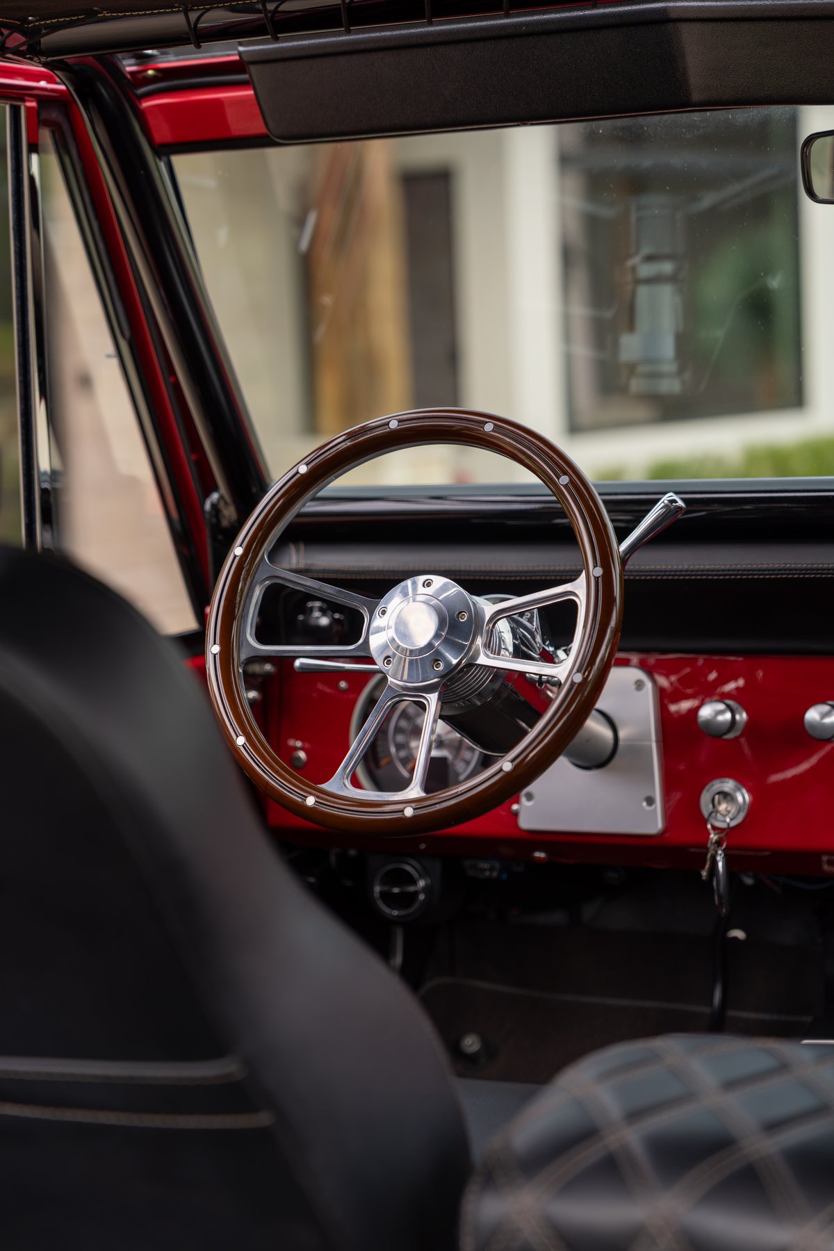 1966 Ford Bronco interior: Wood-rimmed steering wheel, red dashboard trim, and black diamond-stitched seats.