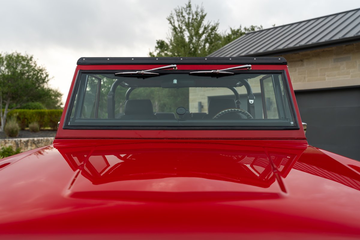 Close-up of a red 1966 Ford Bronco's windshield, hood, and roll cage.