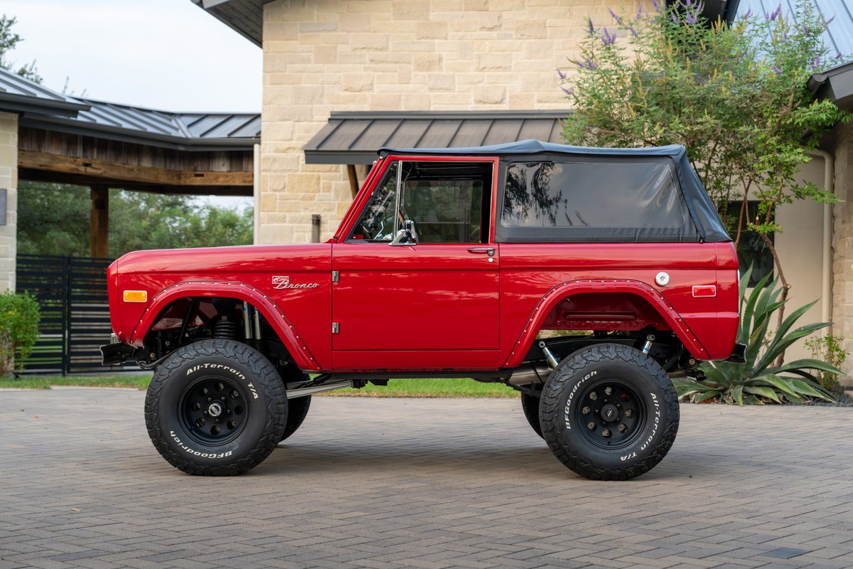 Red 1966 Ford Bronco with black soft top, BFGoodrich All-Terrain tires on black rims.