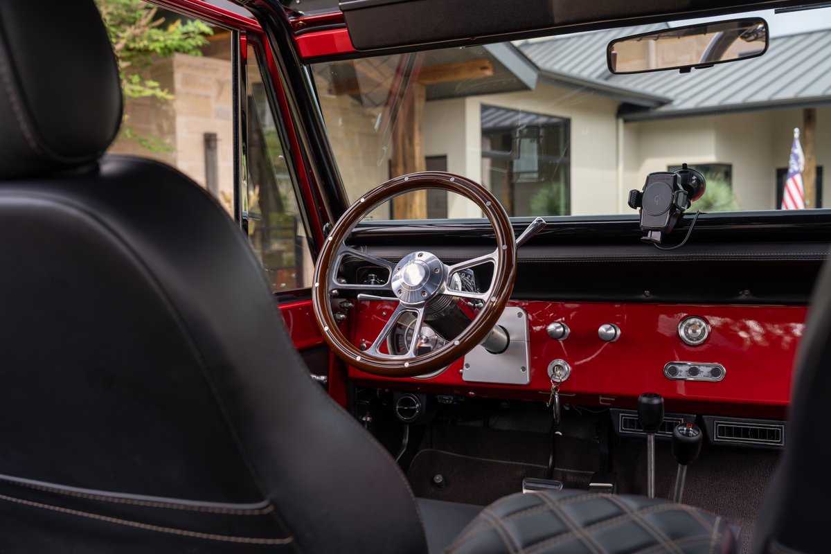Interior of a red 1966 Ford Bronco by Atlas Broncos, featuring a wood-rimmed steering wheel and black leather seats.
