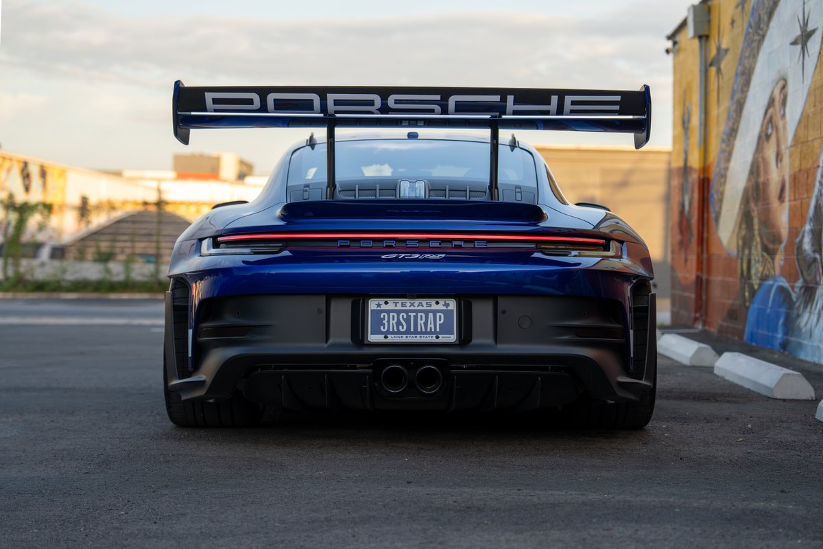 Rear view of a blue 2025 Porsche 911 GT3 RS with a large rear wing and dual exhaust.