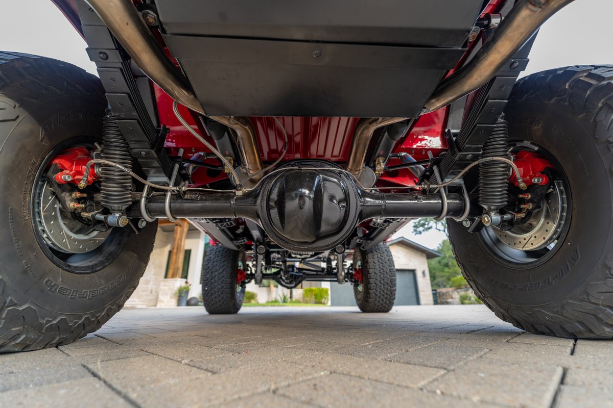 Underneath view of red 1966 Ford Bronco's rear axle, leaf springs, shocks, and drilled rotors.