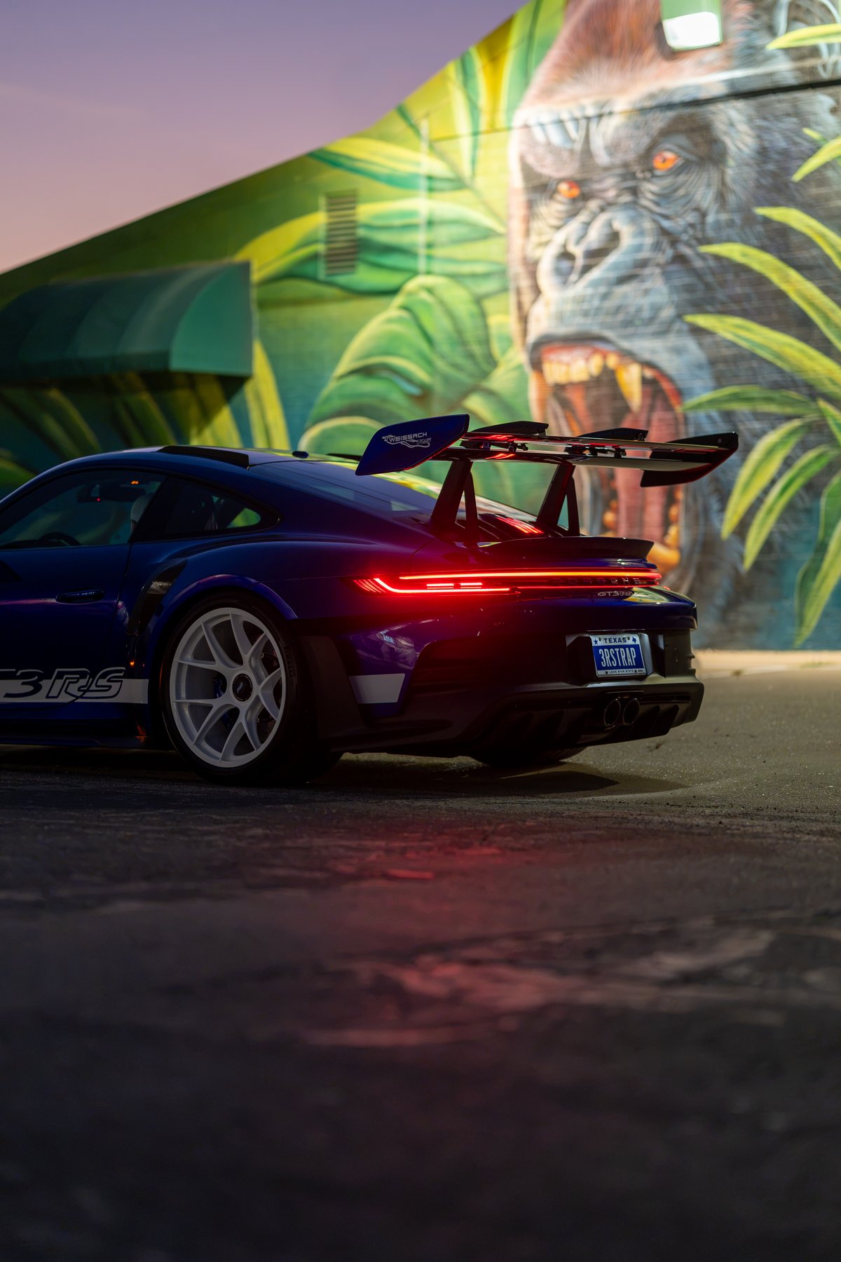 2025 Porsche 911 GT3 RS in purple with white rims, large rear wing, and "3RS" side livery.