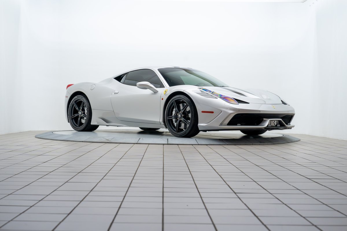 A silver 2015 Ferrari 458 Speciale with black rims is shown on a rotating display.