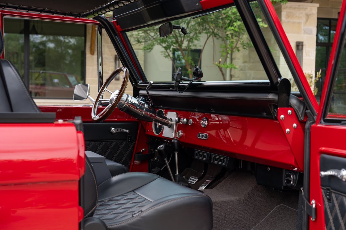Interior of a red 1966 Ford Bronco by Atlas Broncos, featuring a wood-rimmed steering wheel and diamond-stitched black seats.