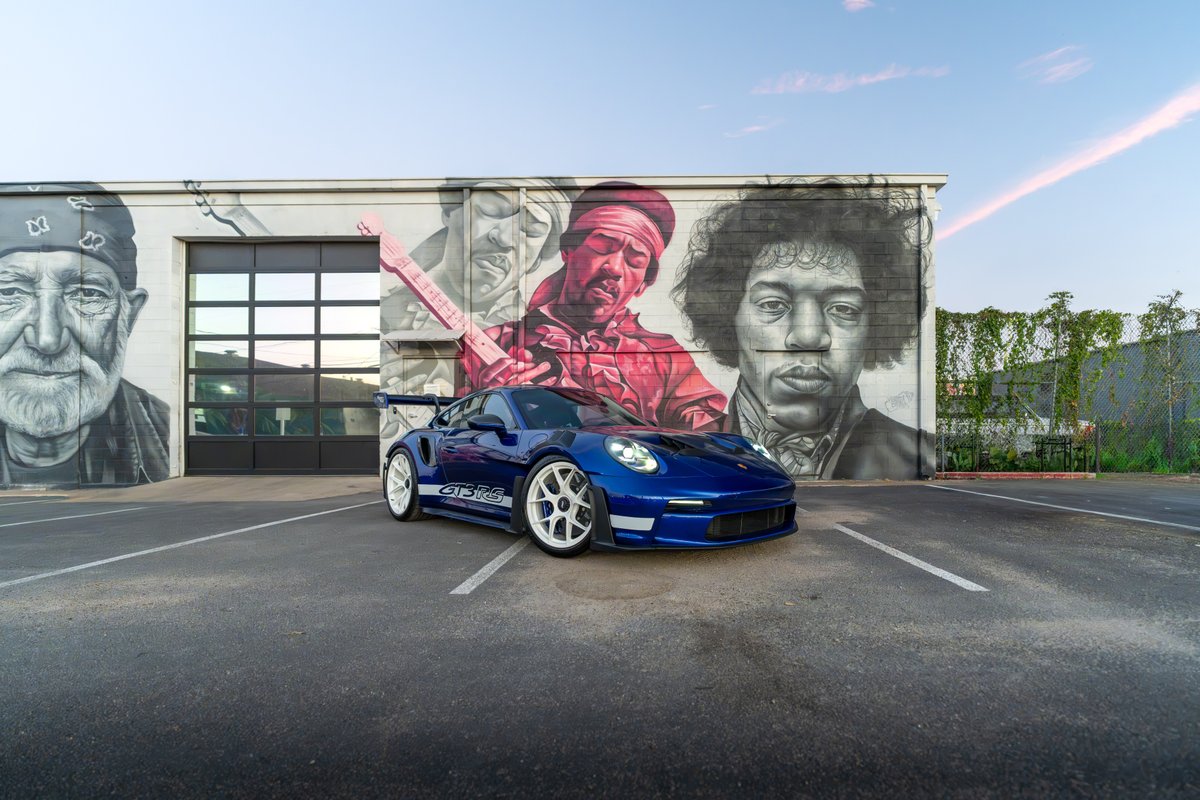 Blue 2025 Porsche 911 GT3 RS with white rims and racing livery parked in front of a mural.