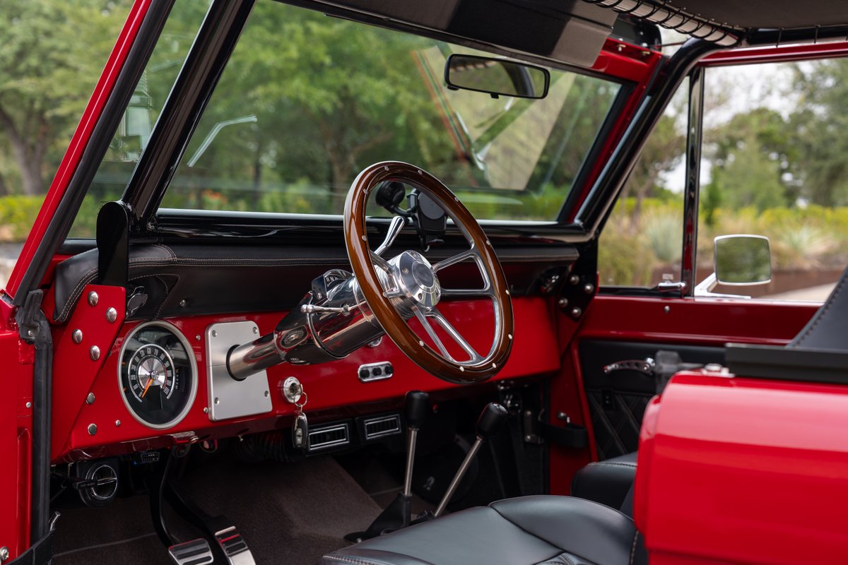 Interior view of a red 1966 Ford Bronco by Atlas Broncos, featuring a wood-rimmed steering wheel.