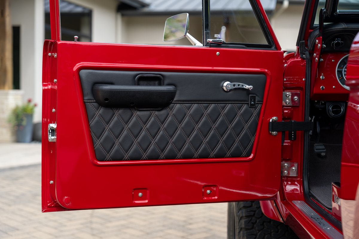 Red 1966 Ford Bronco door interior with diamond-stitched black trim and chrome door handle.
