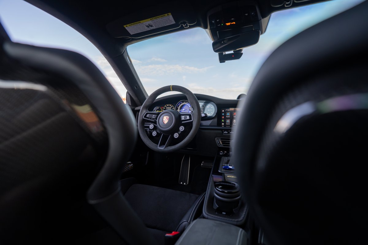 Interior of a 2025 Porsche 911 GT3 RS showing Alcantara steering wheel, carbon fiber trim, and digital gauge cluster.