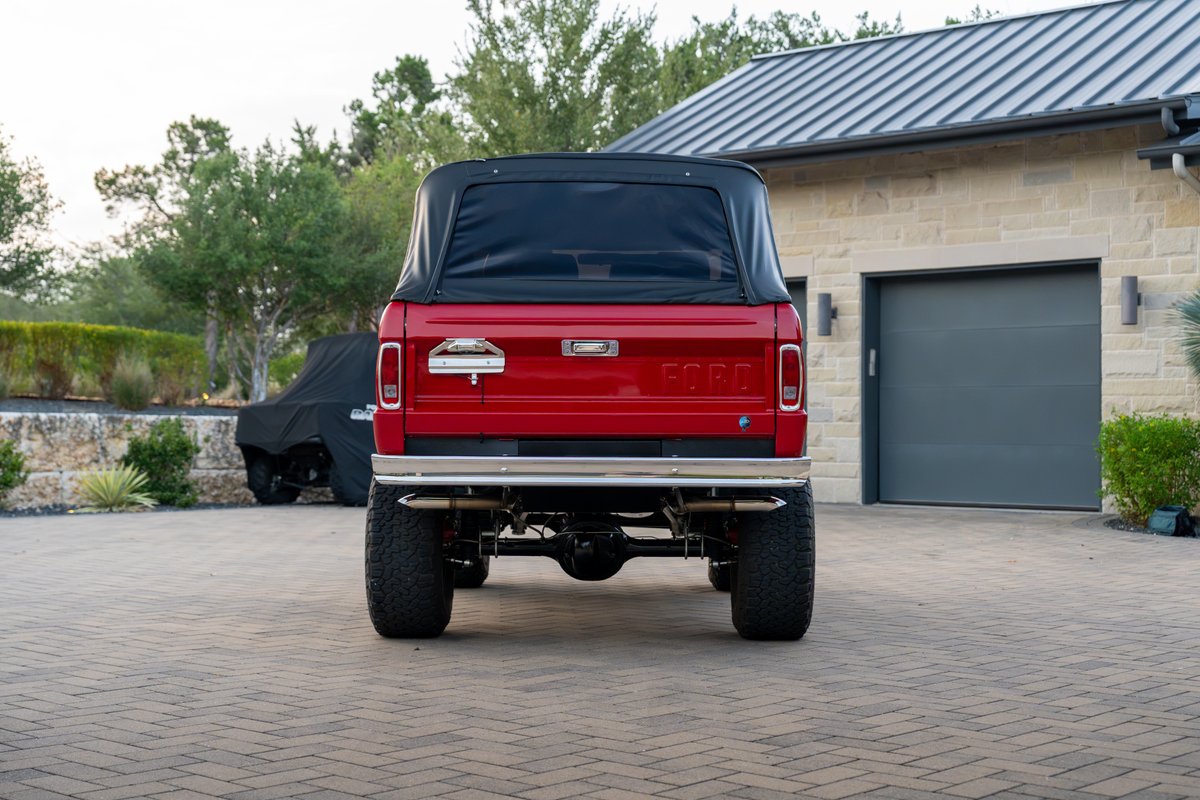 Red 1966 Ford Bronco soft top with chrome bumper and dual exhaust.