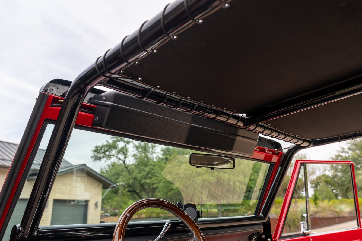 1966 Ford Bronco interior with roll cage, black sunshade, and custom storage.