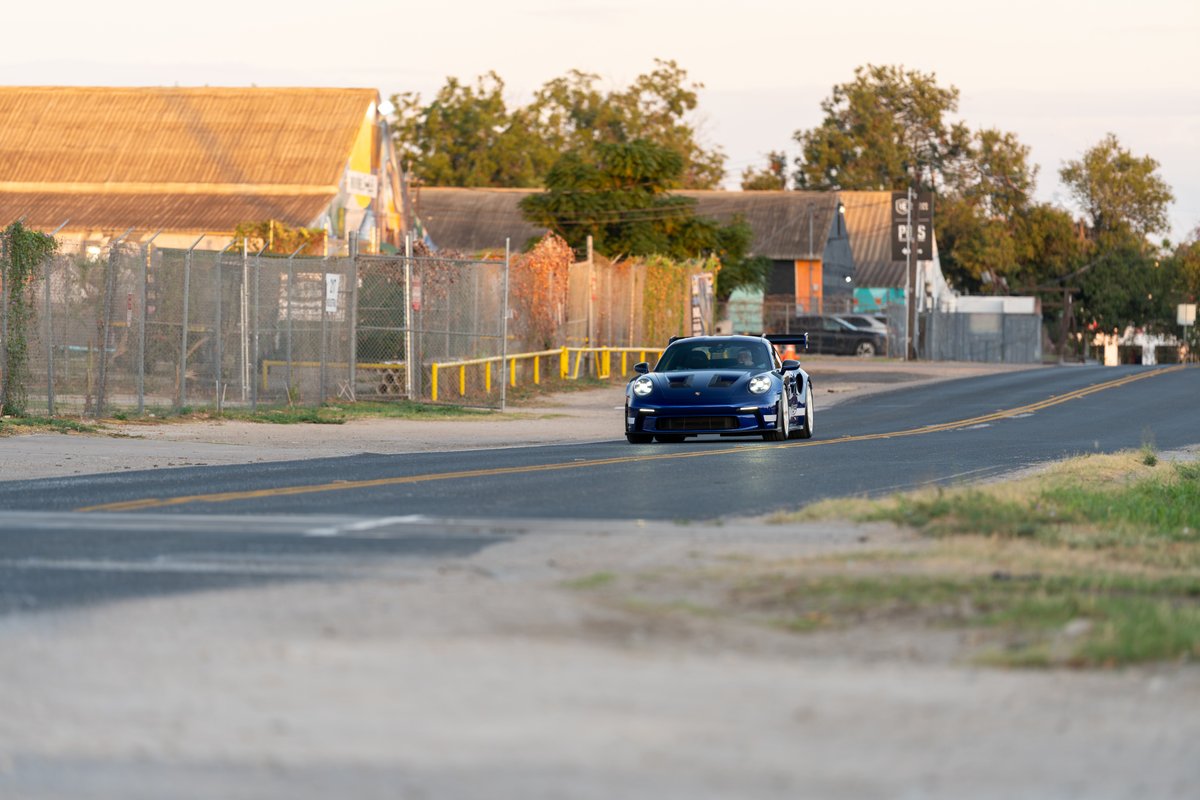 2025 Porsche 911 GT3 RS in blue driving on a road with a large rear wing and white rims.