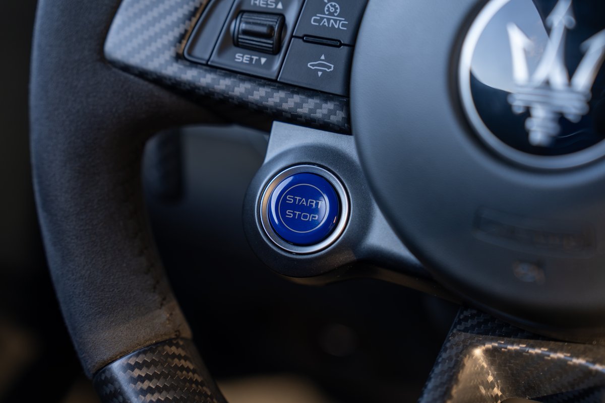 Maserati MC20 steering wheel with blue Start/Stop button and carbon fiber trim.