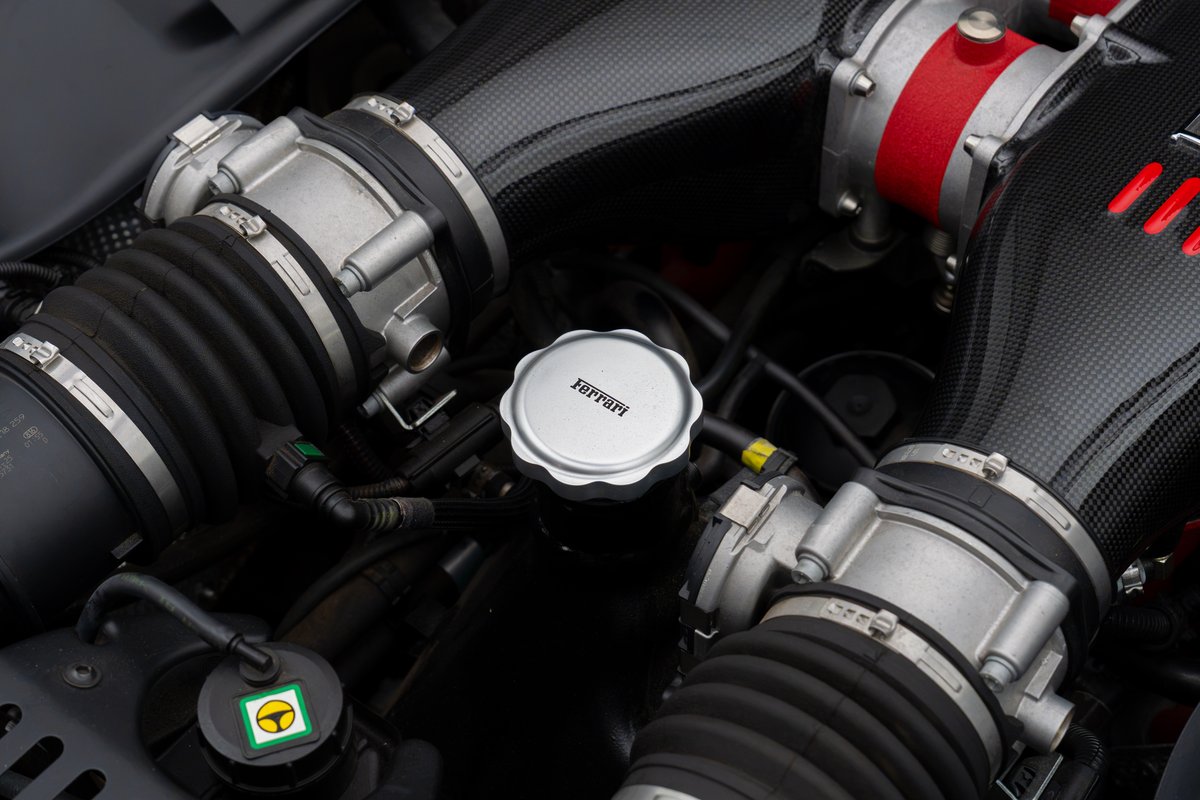 Close-up of the Ferrari 458 Speciale engine bay featuring carbon fiber intake tubes and a Ferrari-branded cap.