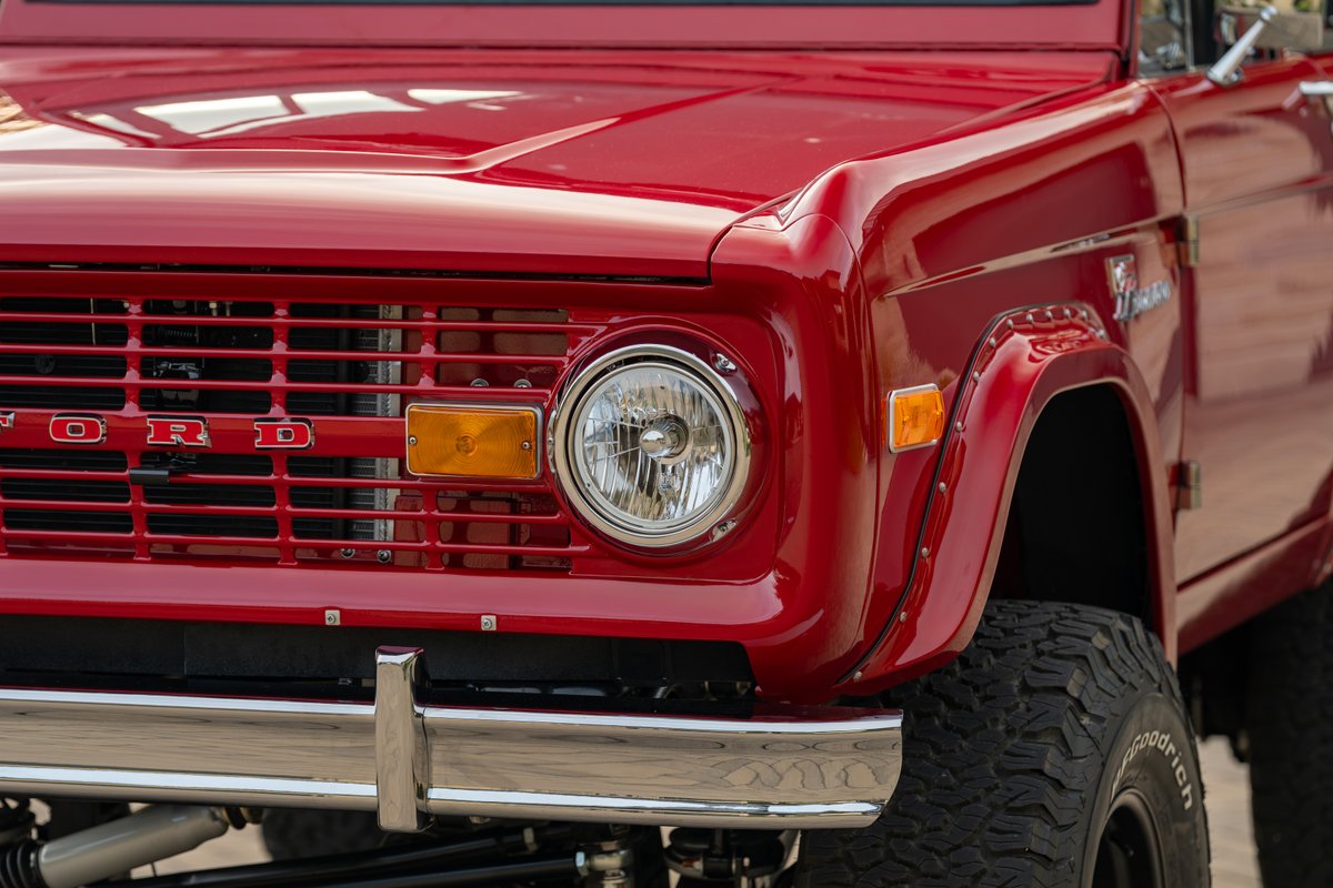 Red 1966 Ford Bronco grille, headlight, chrome bumper, and fender trim.