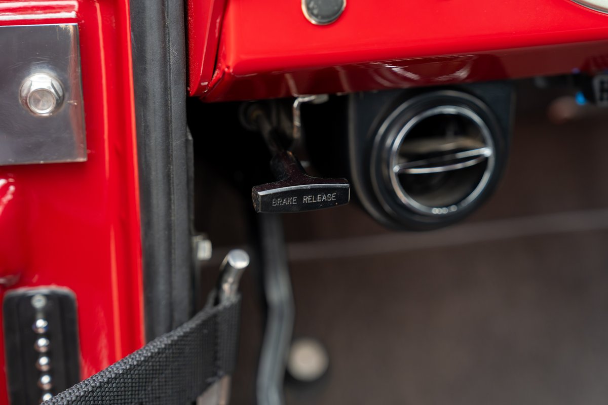 Interior shot of a red 1966 Ford Bronco, showing the brake release lever and a circular vent.