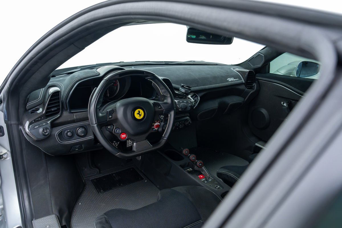 Interior of a 2015 Ferrari 458 Speciale with carbon fiber trim and red start button.