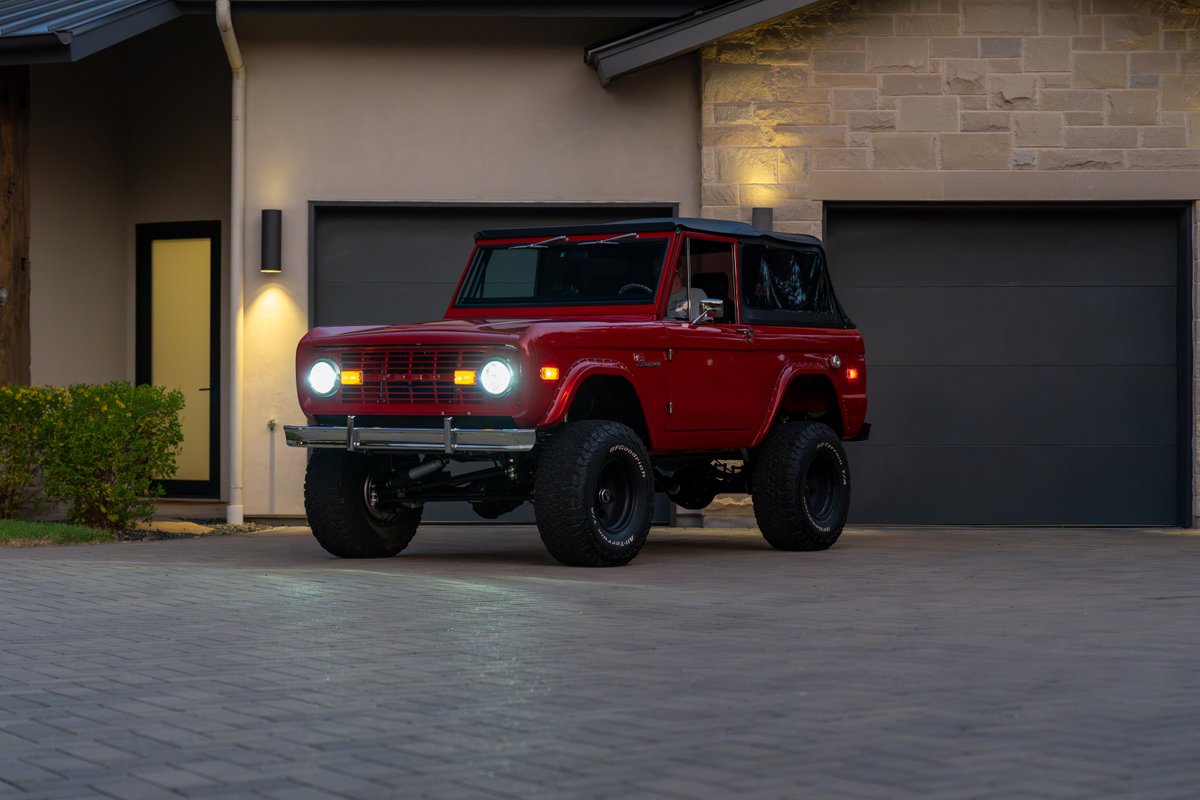 Red 1966 Ford Bronco with black soft top, lifted suspension, and black rims.