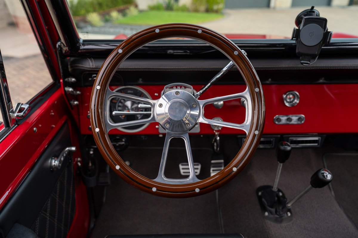 Classic red 1966 Ford Bronco interior with wood-rimmed steering wheel, chrome accents, and floor shifters.