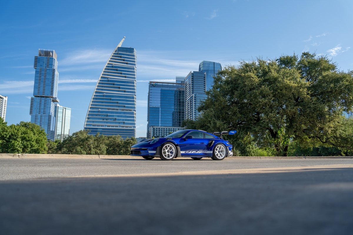 Blue 2025 Porsche 911 GT3 RS with white racing livery and white rims parked on an asphalt road.