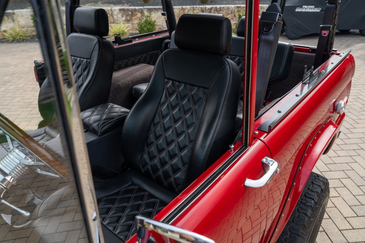 1966 Ford Bronco interior with diamond-stitched black leather seats and red exterior trim.