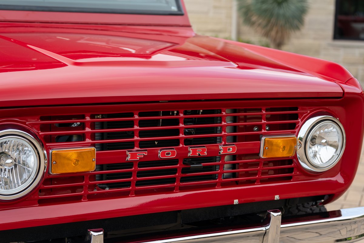 Front view of a red 1966 Ford Bronco grille with chrome trim and headlights.