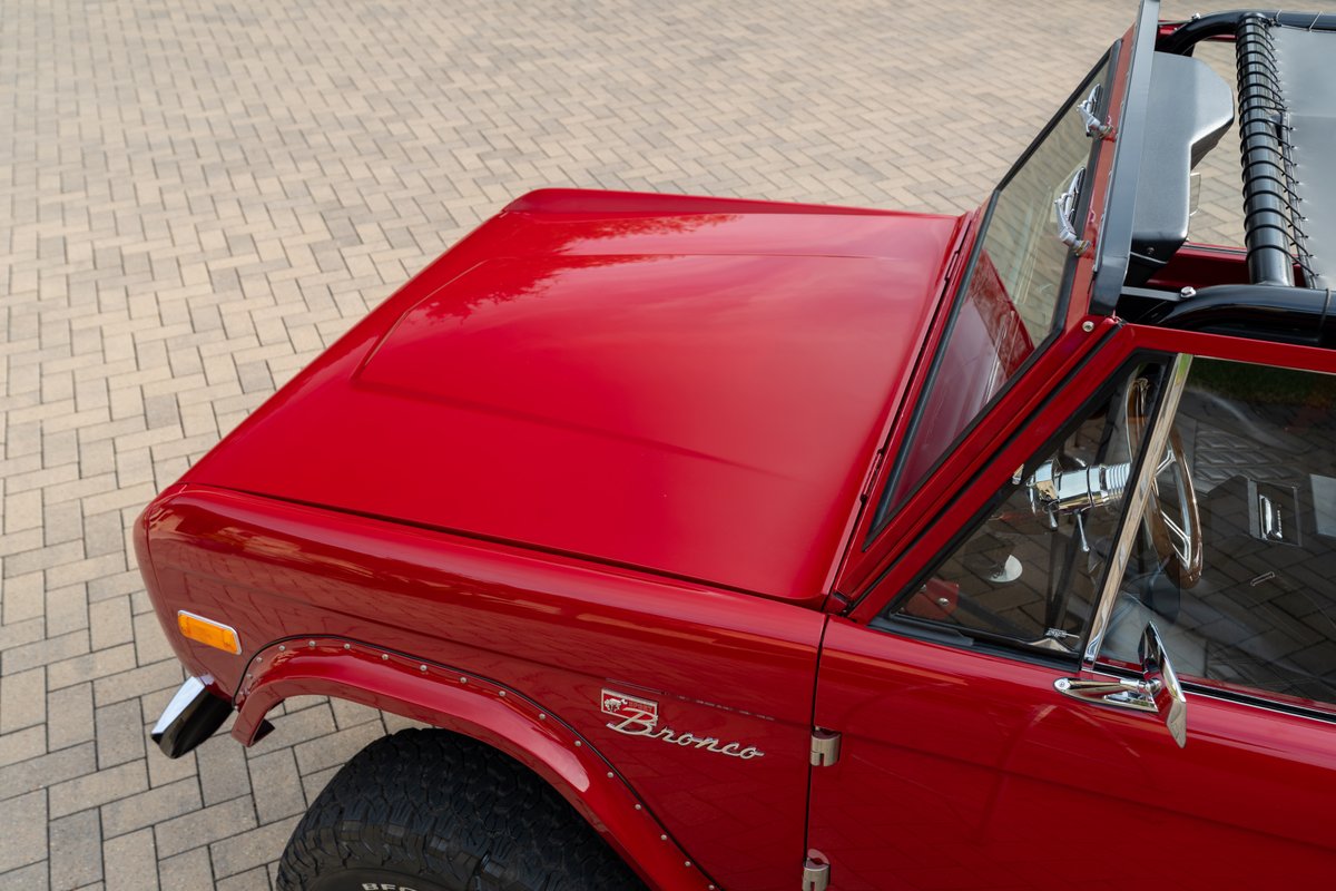 1966 red Ford Bronco's fender and hood with chrome trim and classic Bronco badging.