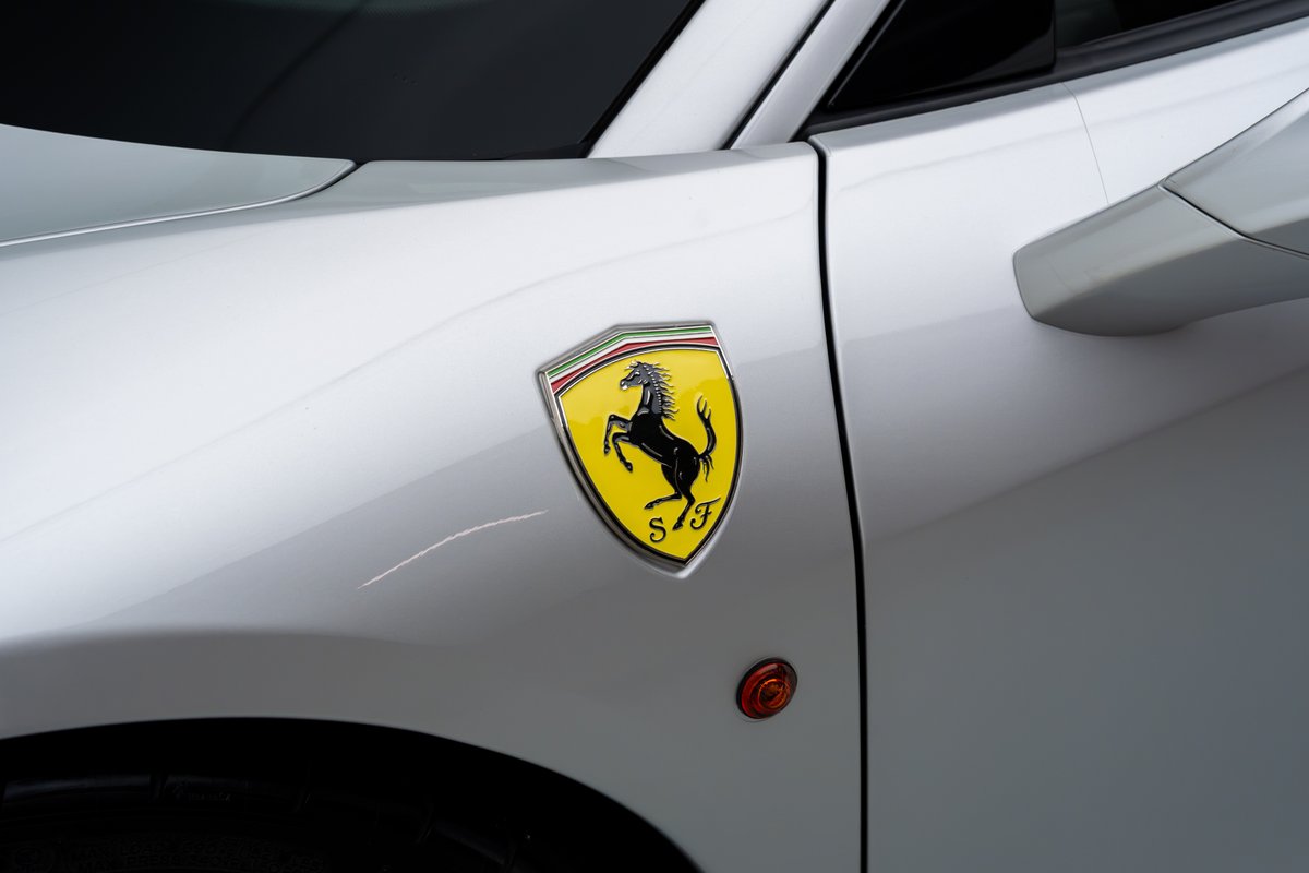 Close-up of a silver 2015 Ferrari 458 Speciale's iconic yellow Scuderia Ferrari badge and side marker light.