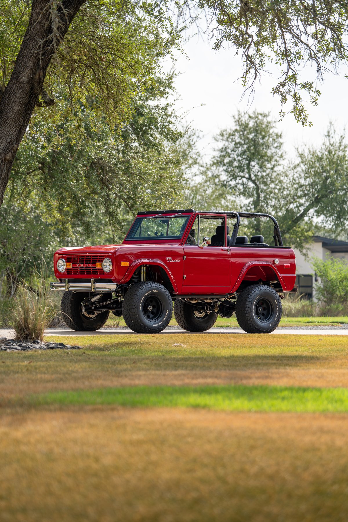 1966 red Ford Bronco by Atlas Broncos, lifted suspension, black rims, off-road tires.